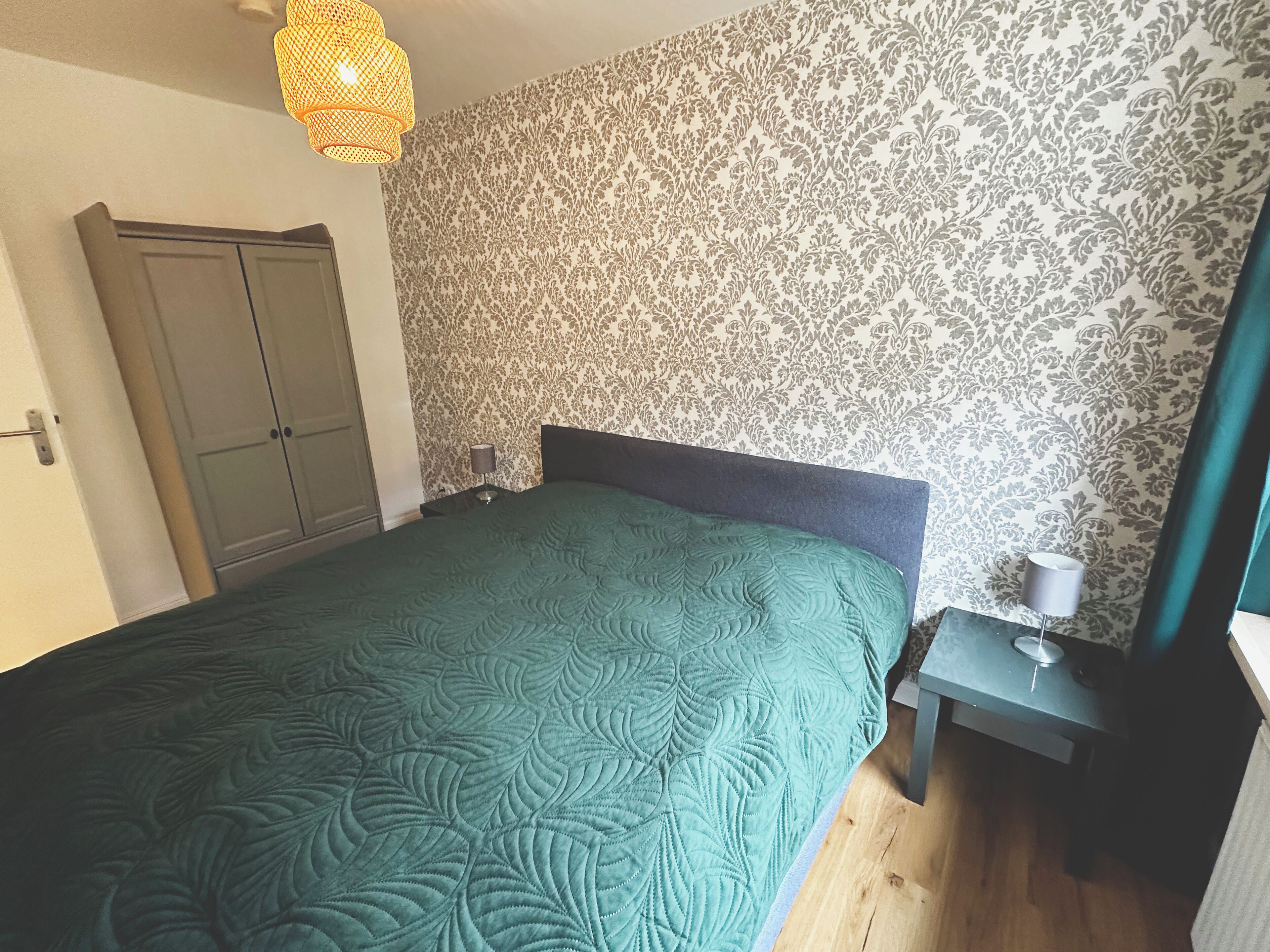 Une chambre à coucher comprenant un lit, une table de chevet, une lampe, une armoire et un papier peint à motifs.