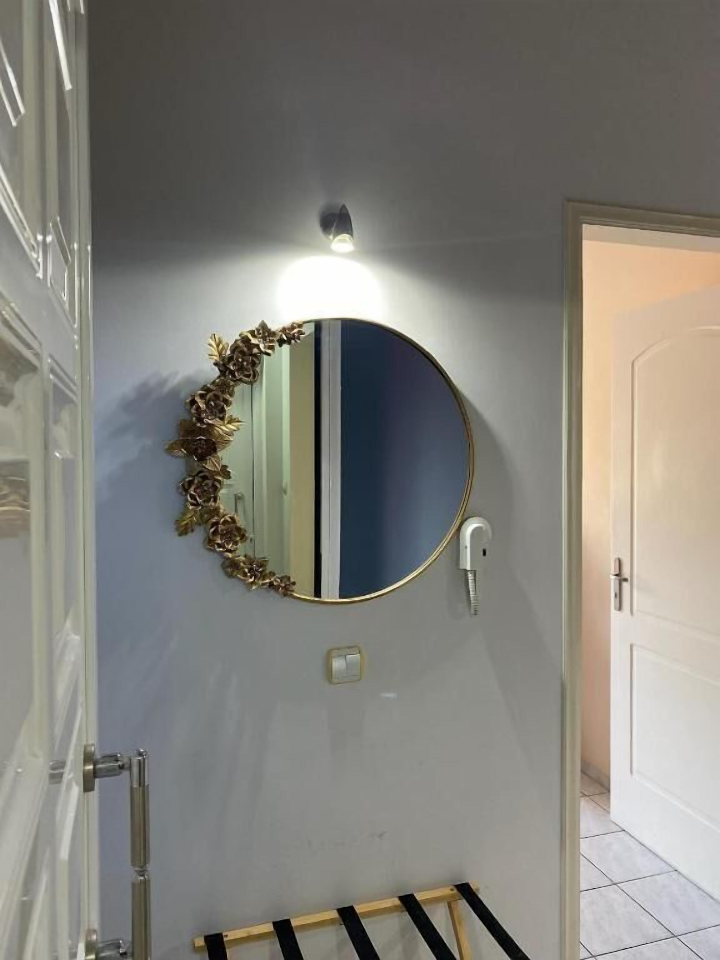 Une salle de bain avec un miroir rond, un luminaire fixé au mur et un porte-serviettes.