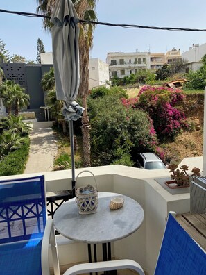A balcony with a table, chairs, a hanging cloth, and a view of buildings and greenery. - Rethymno Blue Residence (Rethymno)