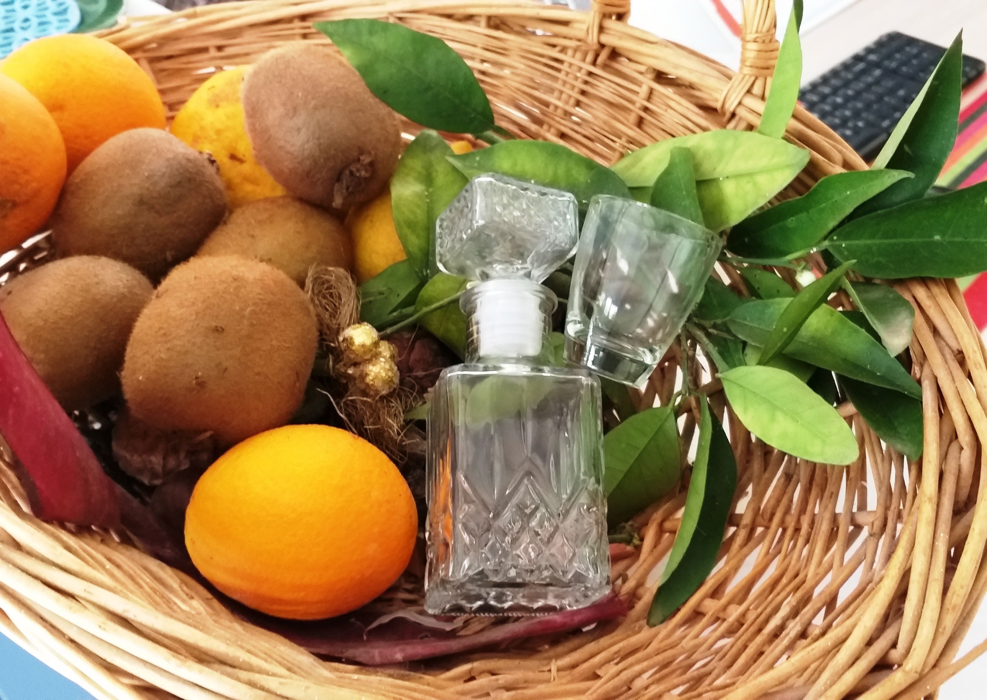 Un panier en osier contenant des kiwis, des oranges et une petite bouteille en verre.