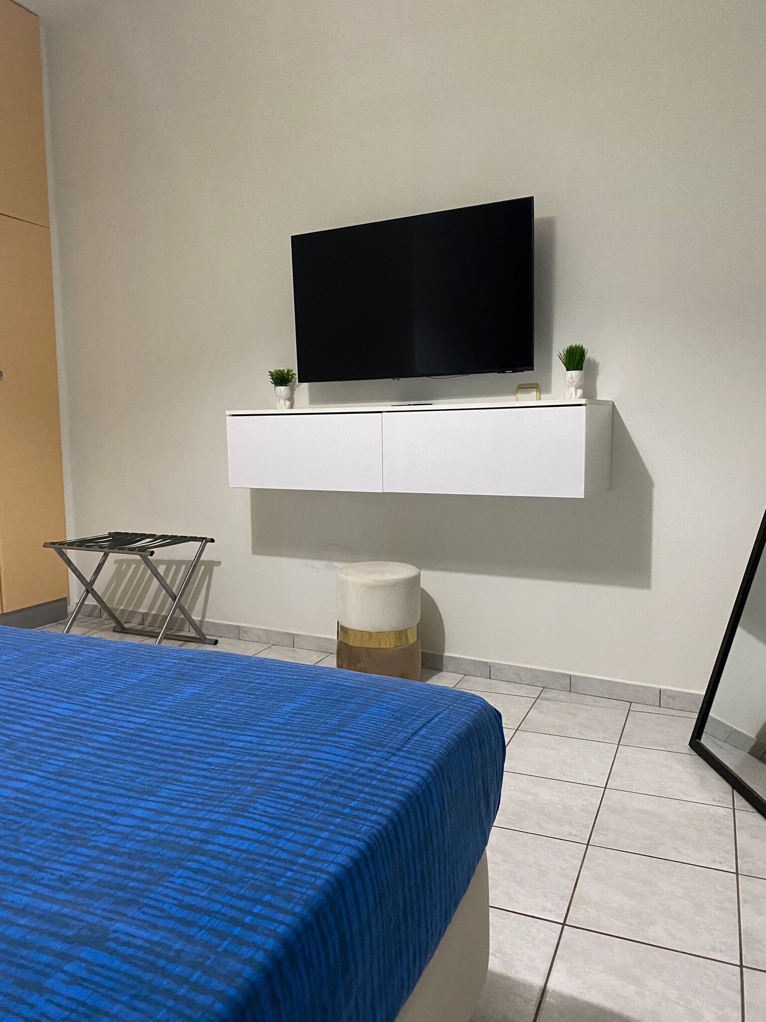 Ein Schlafzimmer mit einem Bett, einem an der Wand montierten Fernseher, einem kleinen Hocker und einem Wäscheständer.