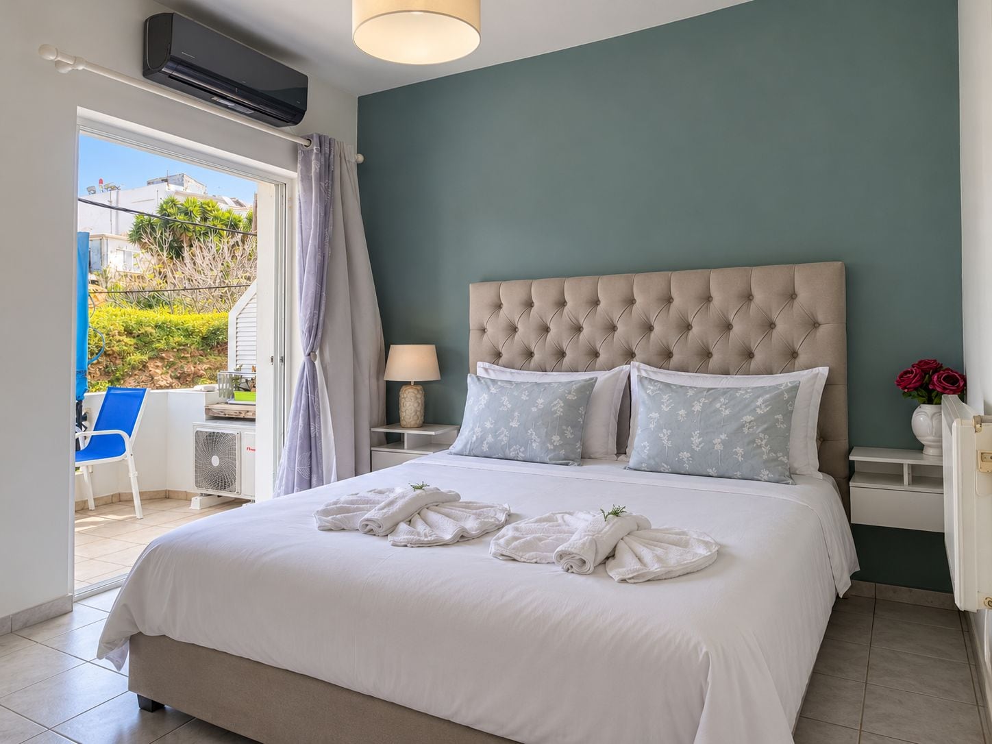 Une chambre à coucher avec un grand lit, une tête de lit, une table de chevet, une lampe et une vue sur l’extérieur.
