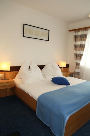 Ein Hotelzimmer mit einem Bett, zwei Nachttischlampen, einem gerahmten Bild an der Wand und einem Fenster mit Vorhängen.