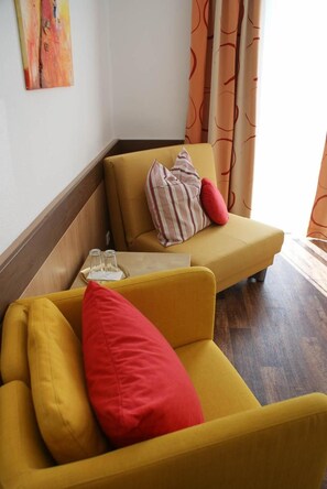 A yellow sofa with red and striped pillows, a small table with glasses and a napkin, and a painting on the wall.