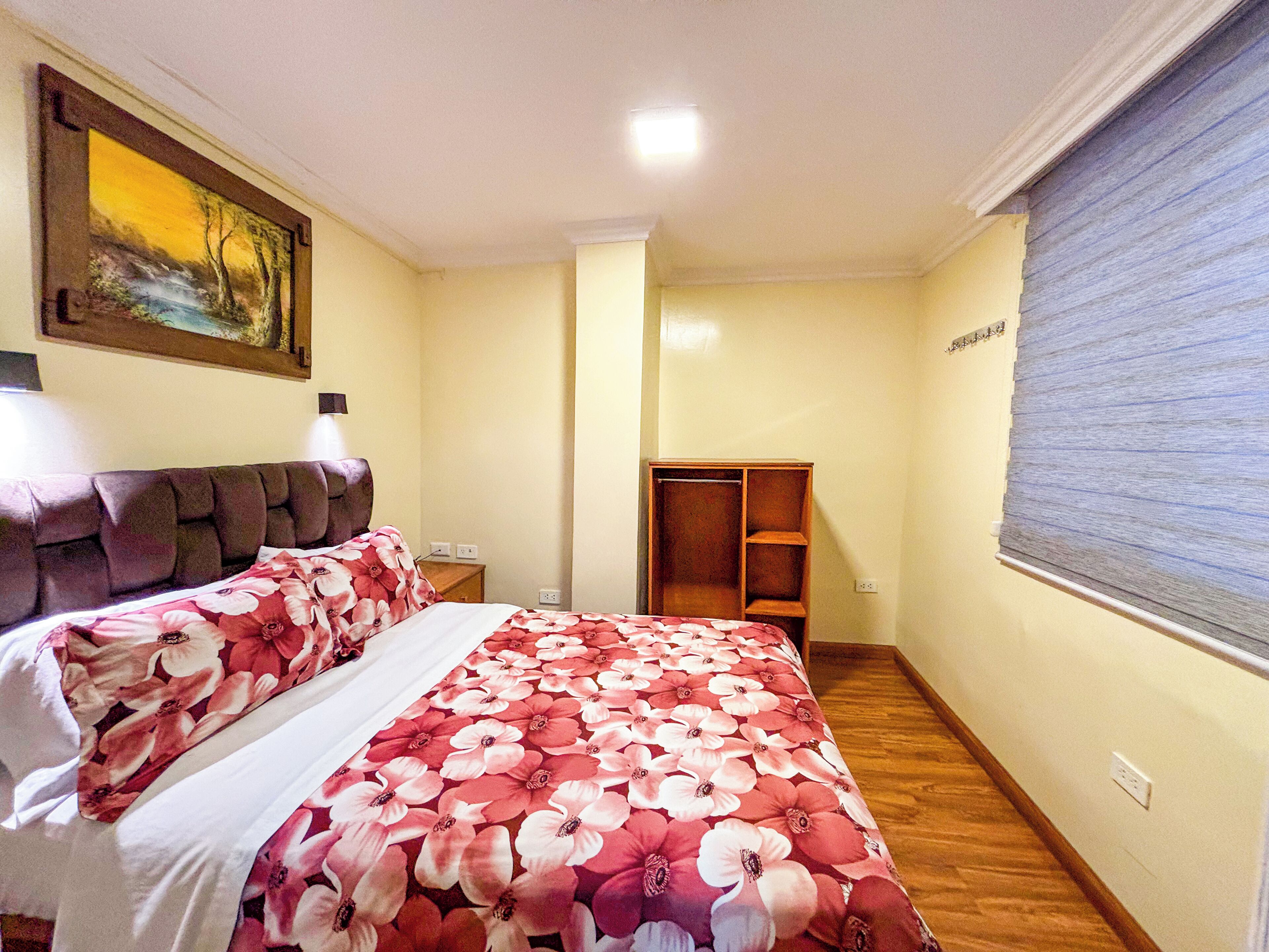 A bedroom with a bed, a nightstand, a wardrobe, and a painting on the wall.