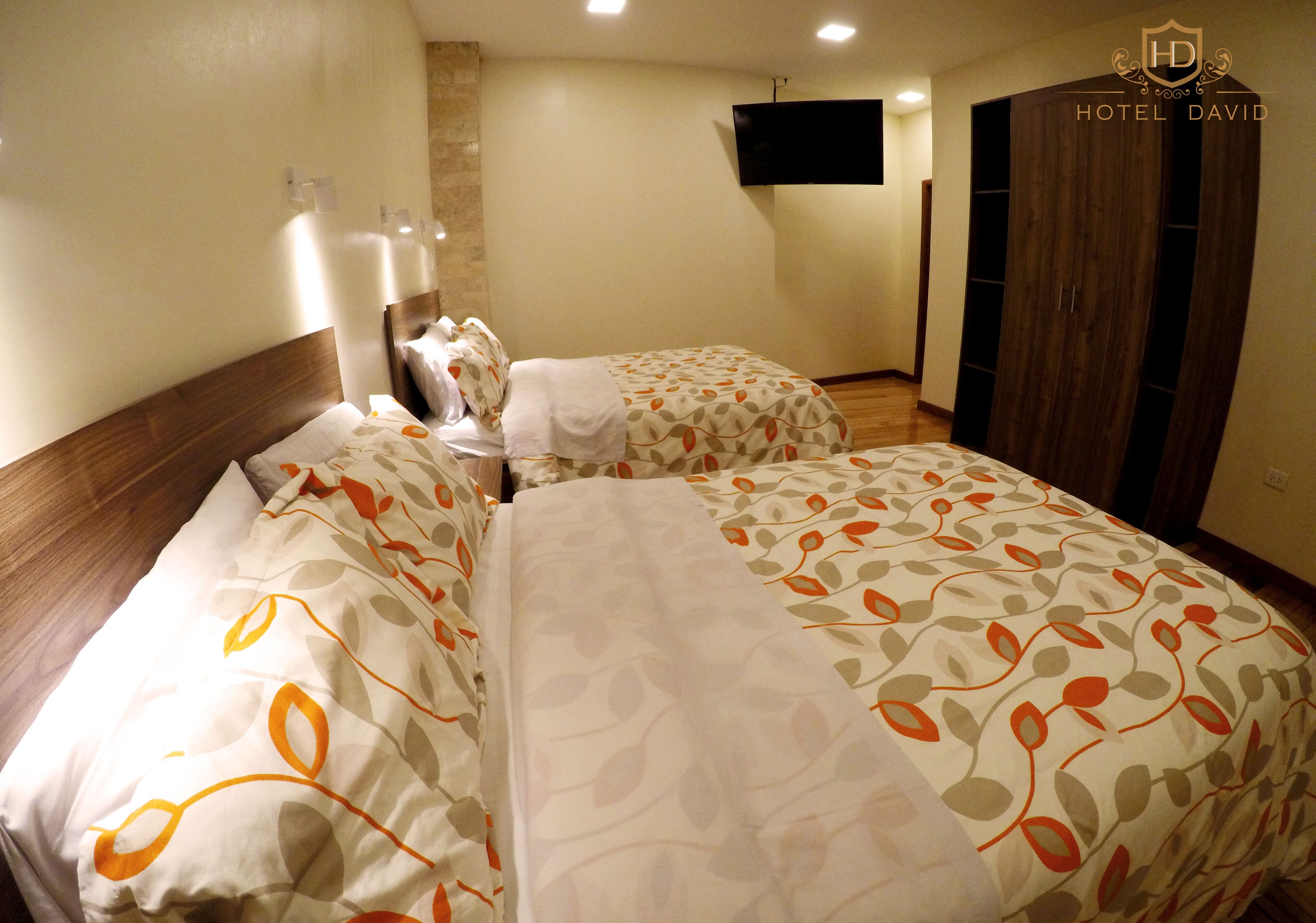 Ein Hotelzimmer mit zwei Betten, einem an der Wand befestigten Fernseher und einem Kleiderschrank.