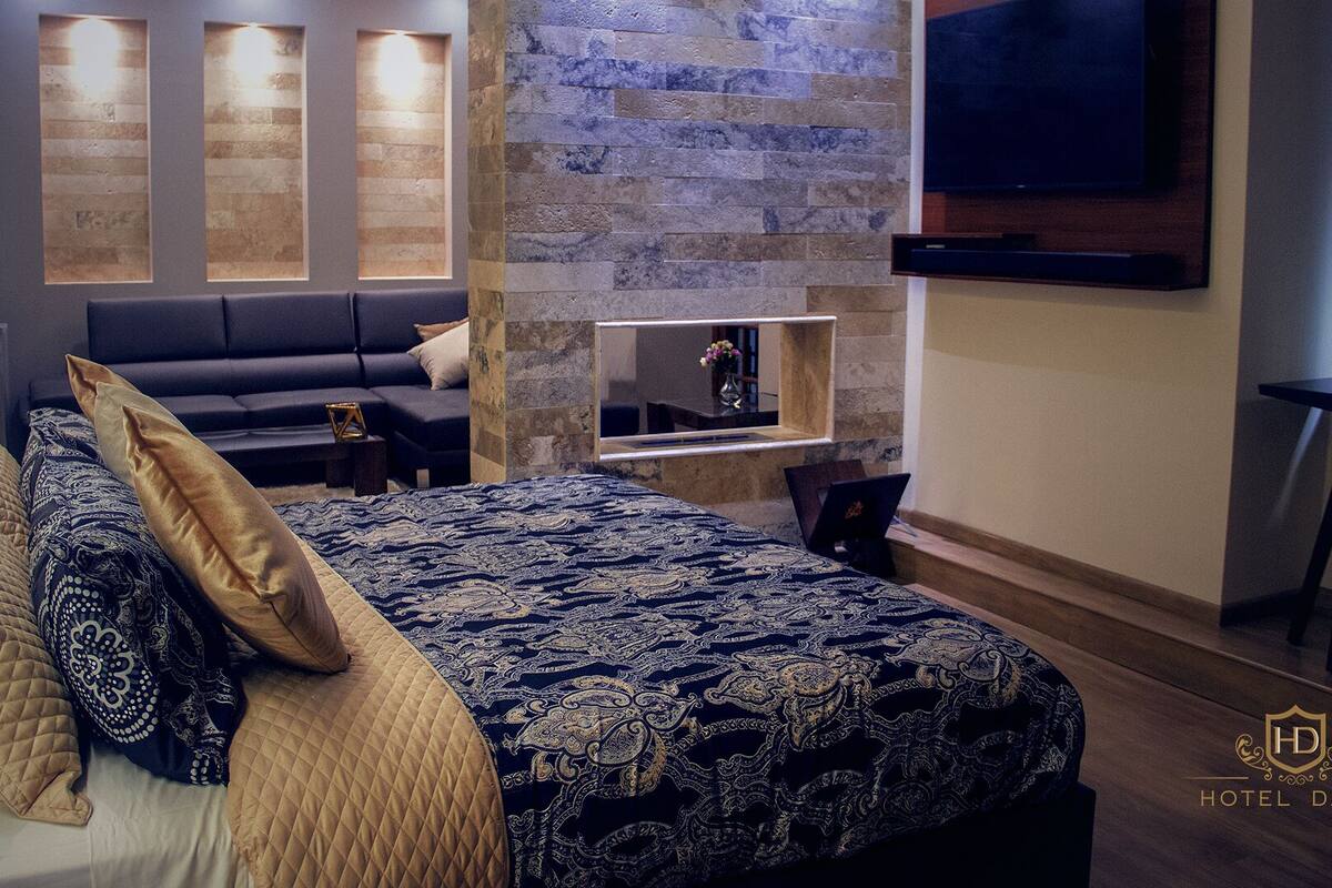Quarto de hotel com uma cama grande, um sofá, uma TV e uma pequena mesa.