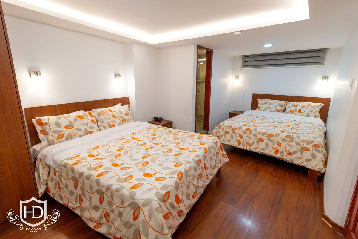 Quarto de hotel com duas camas, piso de madeira e um aparelho de ar condicionado na parede.
