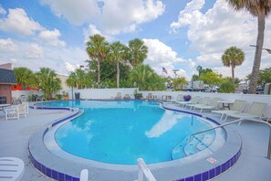 A swimming pool with a blue tiled edge, surrounded by lounge chairs and palm trees.