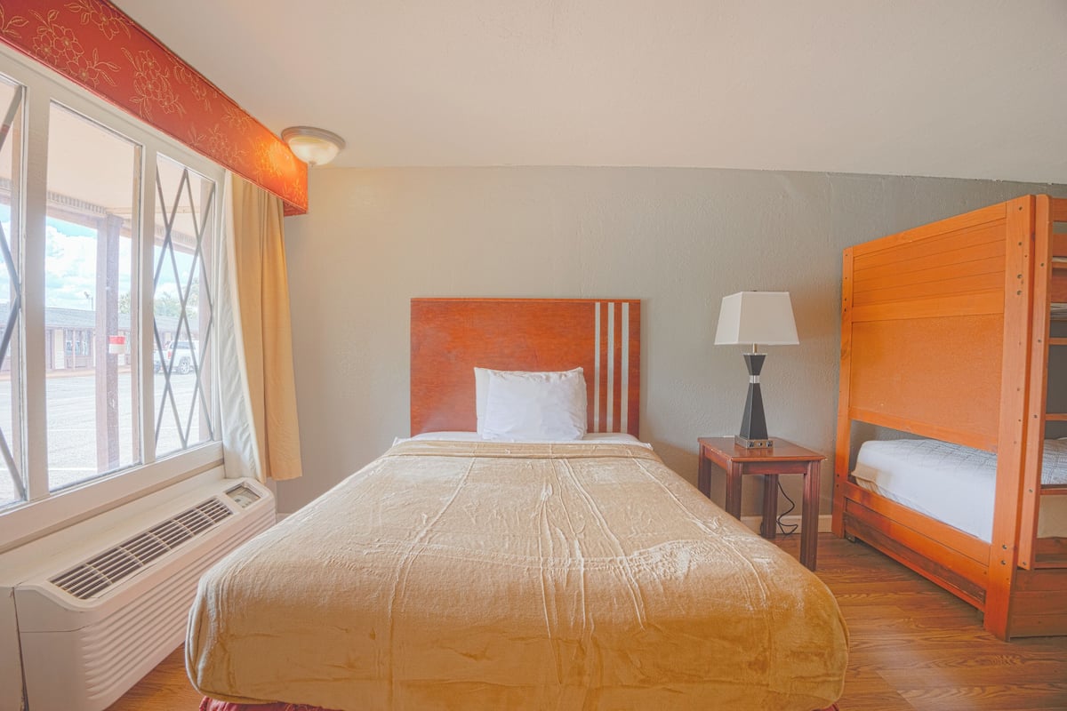 Ein Hotelzimmer mit einem Bett, einem Heizgerät, einem Fenster, einem Nachttisch mit Lampe und einem Stockbett.