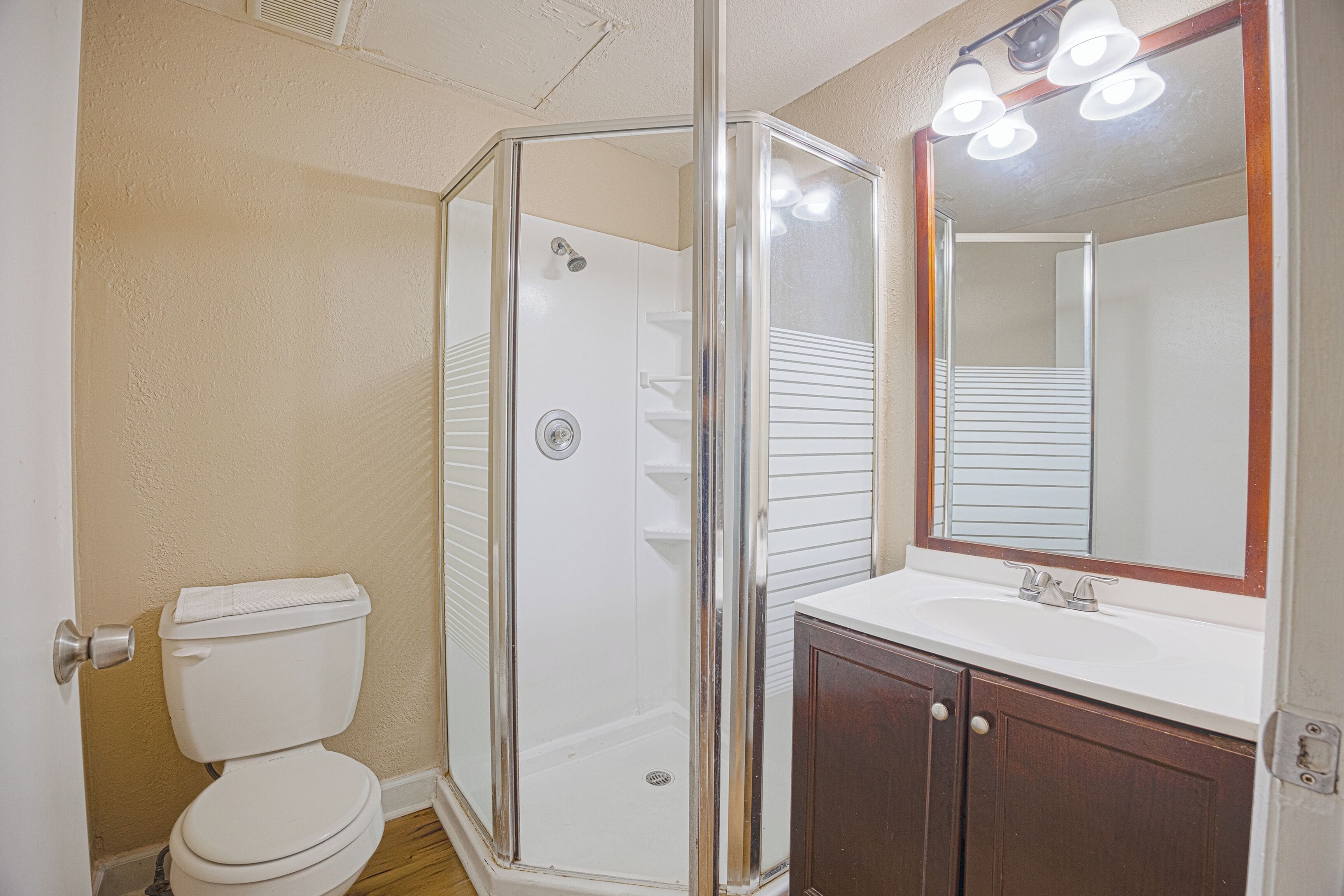 A bathroom with a glass shower enclosure, a white toilet, a wooden vanity with a mirror, and a sink.