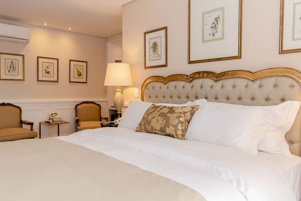 Una habitación de hotel con una cama grande, una silla, una mesita de noche y cuadros en la pared.