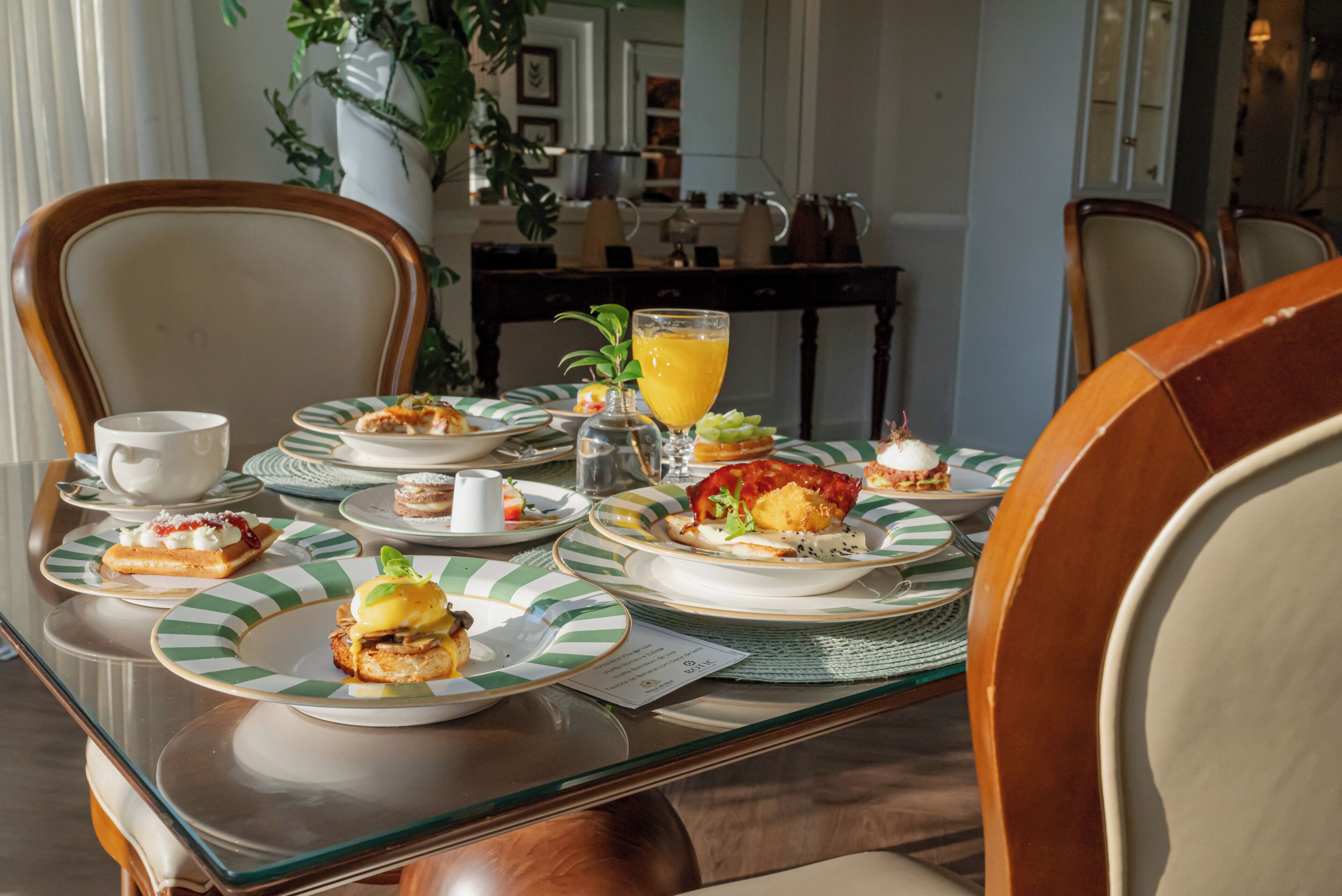 Une table à manger avec des assiettes remplies de nourriture, un verre de jus d’orange et une théière.