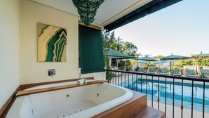 Un área de spa con una bañera grande, un banco de madera y vistas a una piscina con sillones y sombrillas.