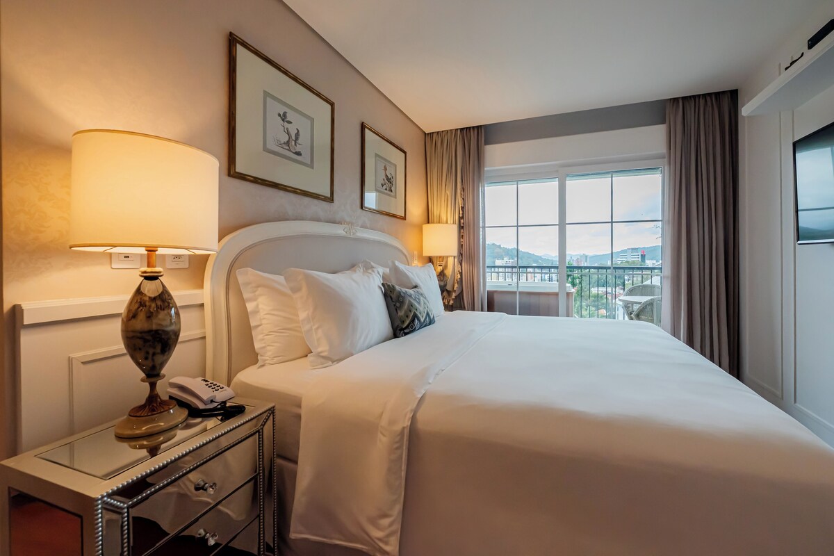 A hotel room with a large bed, bedside lamps, a telephone, a glass table, and framed artwork on the wall.