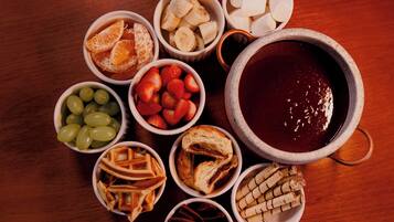 Diversos alimentos, entre ellos frutas, pan y un tazón grande con un líquido oscuro, probablemente una bebida, dispuestos sobre una mesa de madera.