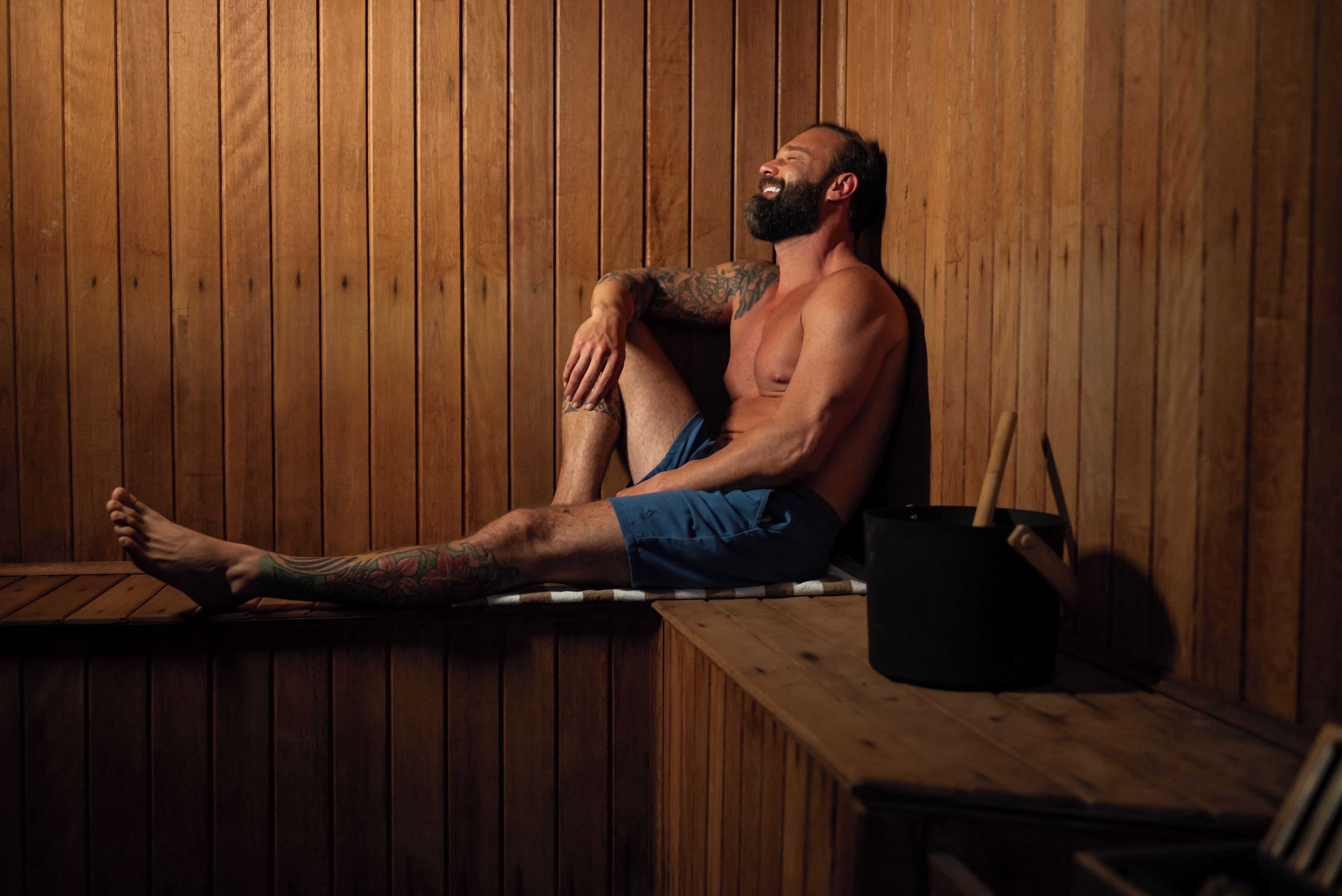 Eine Person sitzt in einer hölzernen Sauna mit einer Sitzbank und einem Topf auf einem Tisch.