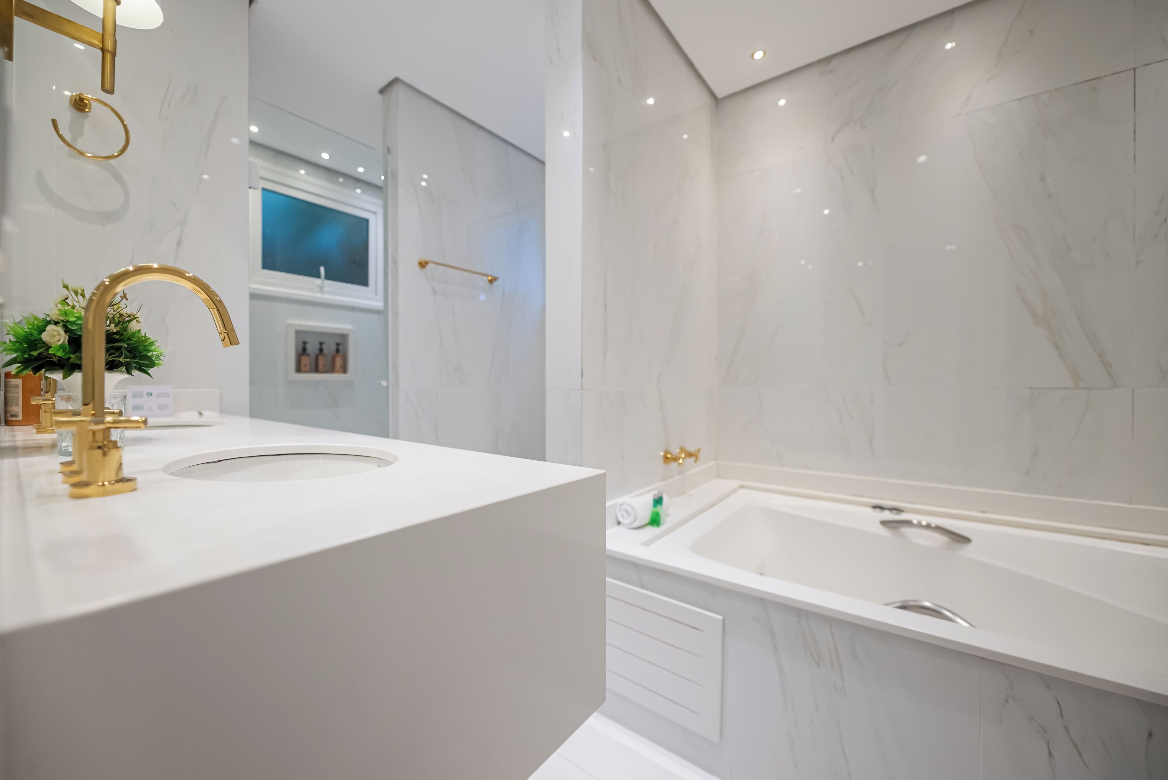 A modern bathroom with a white vanity, gold fixtures, a large bathtub, and marble walls.
