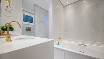 A modern bathroom with a white vanity, gold fixtures, a large bathtub, and marble walls.