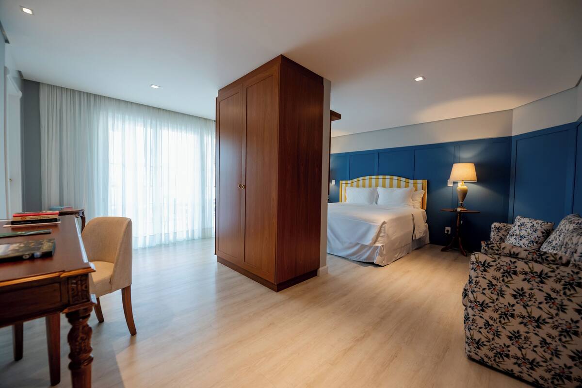 Una habitación de hotel con cama, escritorio, armario, sofá y lámpara.