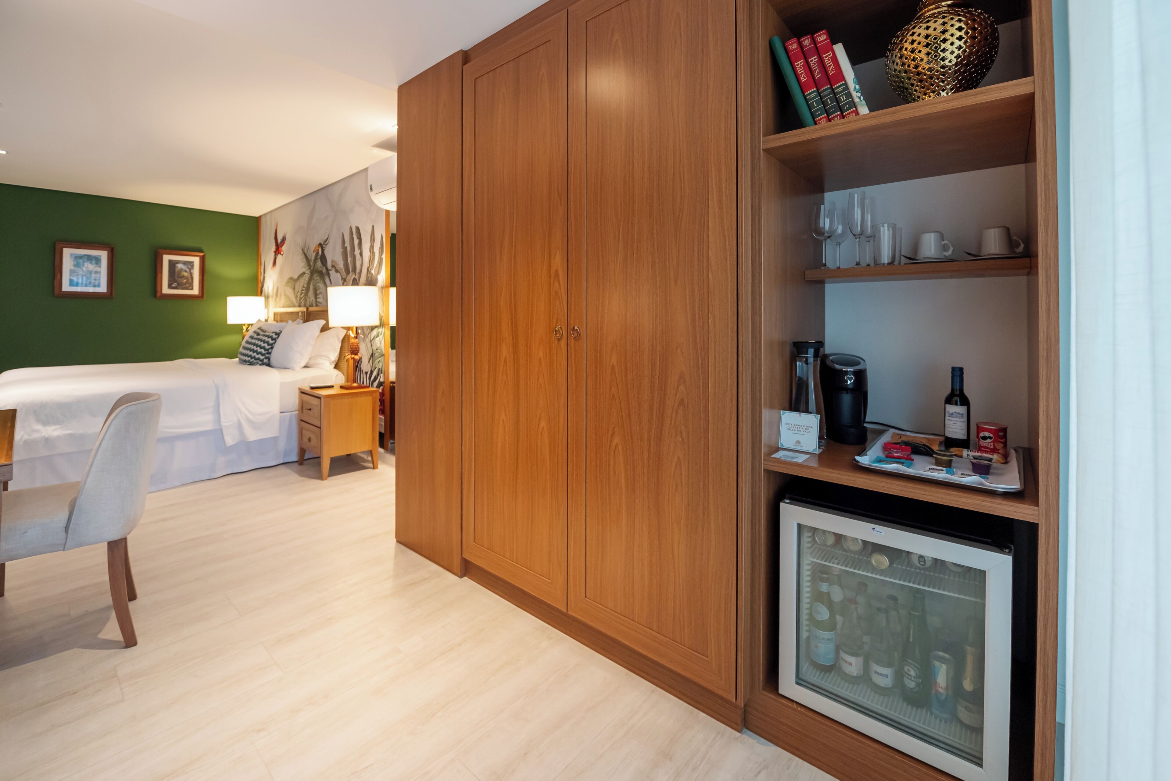 A hotel room with a bed, bedside table, lamp, wardrobe, and a minibar.