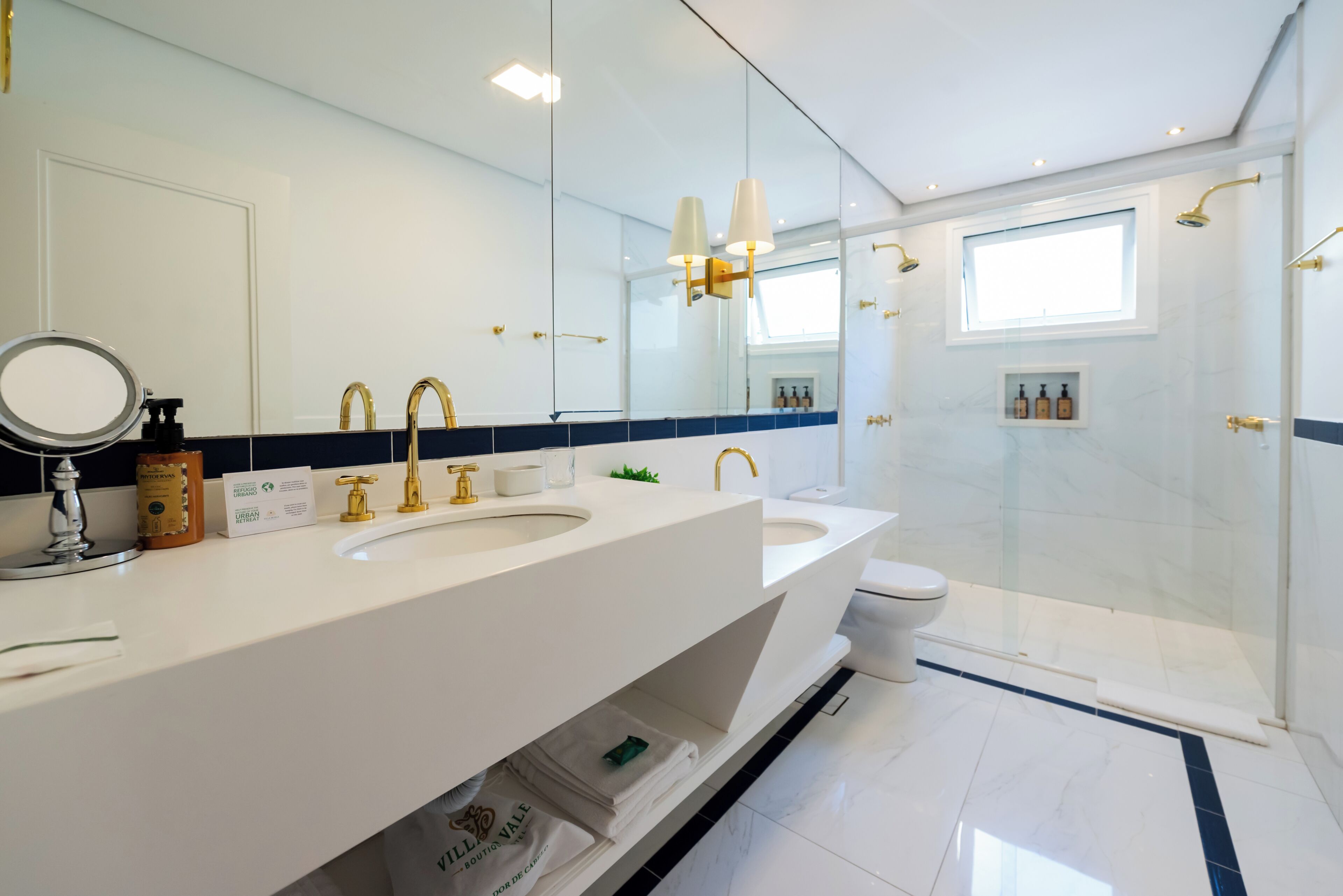 A modern bathroom with a double sink, a toilet, a glass shower enclosure, and a large mirror.