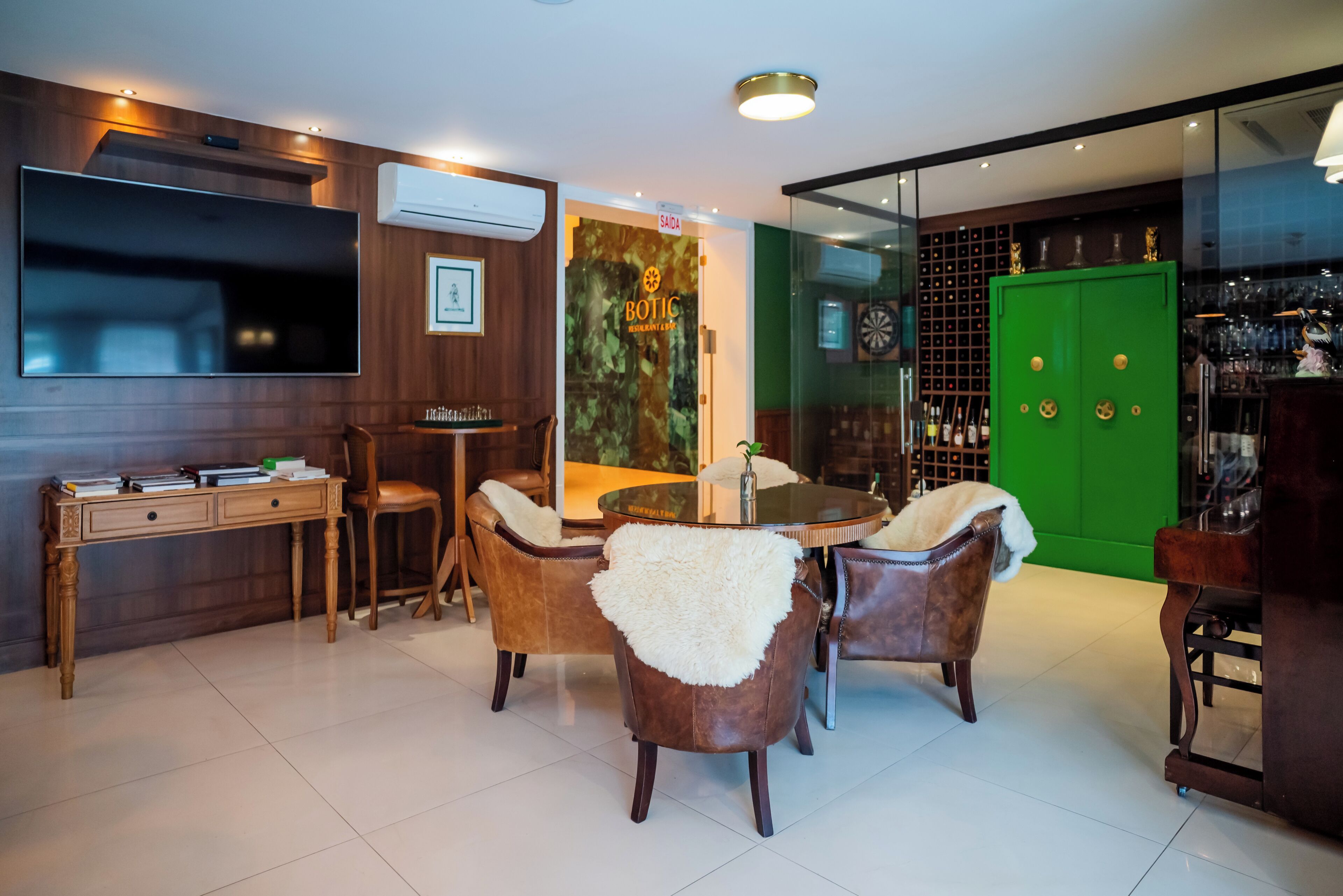 A modern dining area with leather chairs, a round table, a TV, and a green cabinet with trophies.
