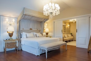 A large, elegantly furnished bedroom with a canopy bed, a bench, and a chandelier.