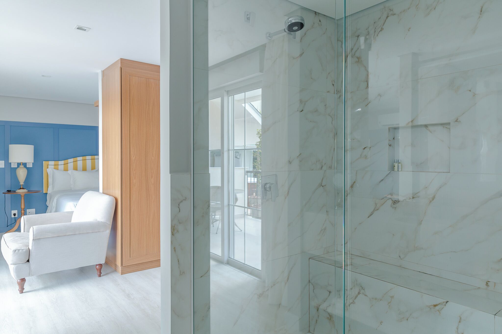 Un baño moderno con cabina de ducha de vidrio, una silla blanca y un mueble de madera.