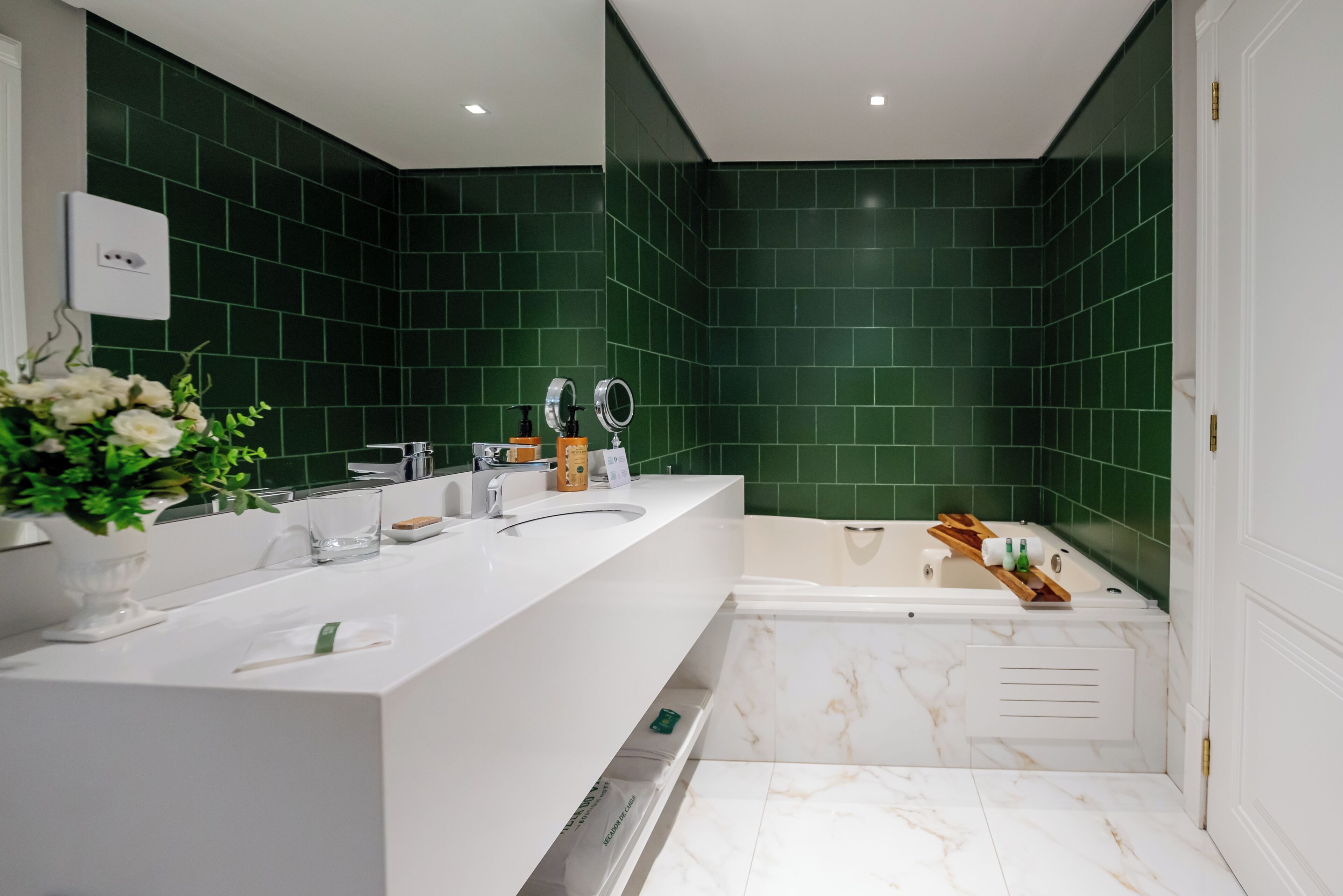 Um banheiro moderno com toucador branco, banheira e paredes com azulejos verdes.
