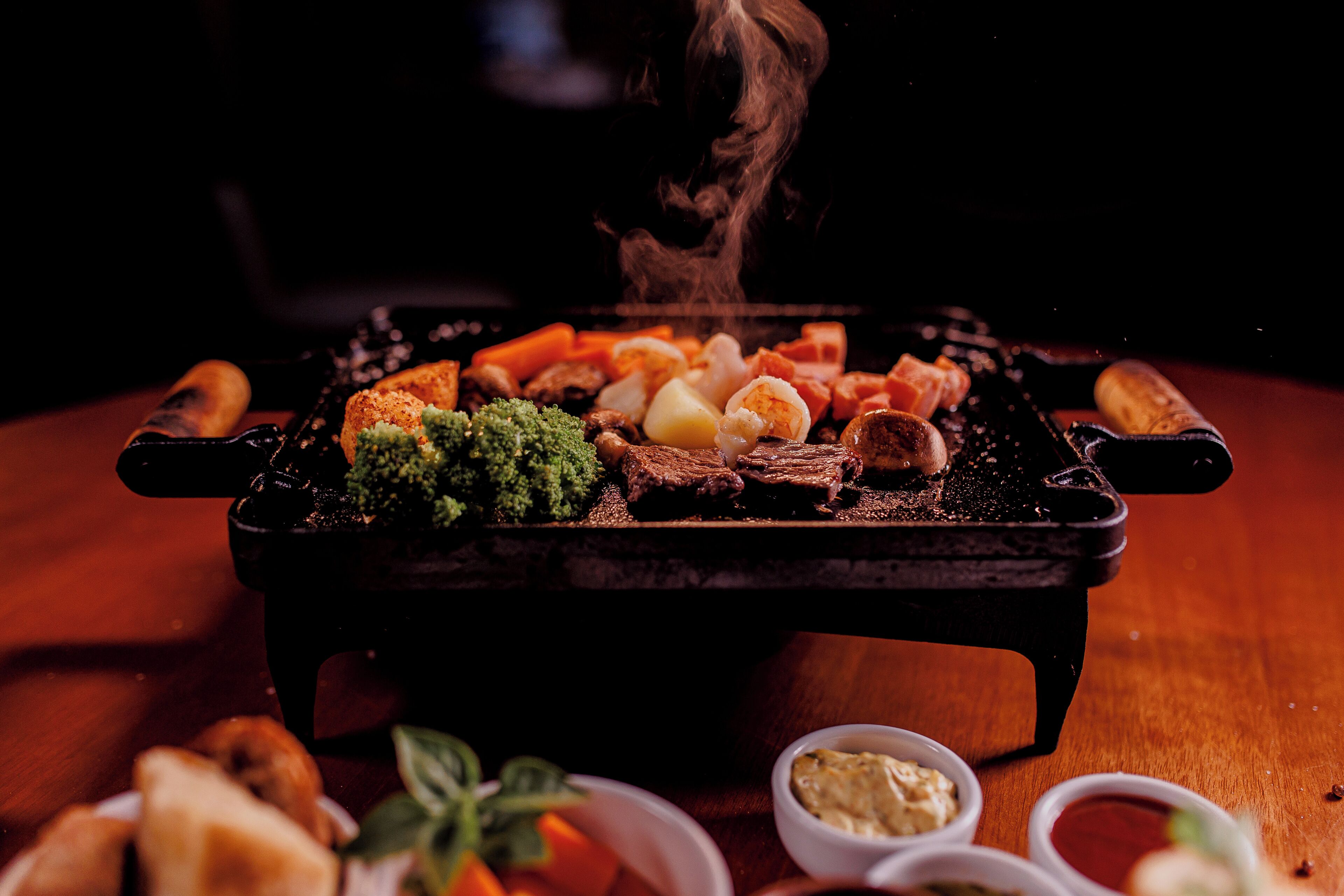 Una barbacoa amb diferents carns i verdures, acompanyada de petits recipients de salses.