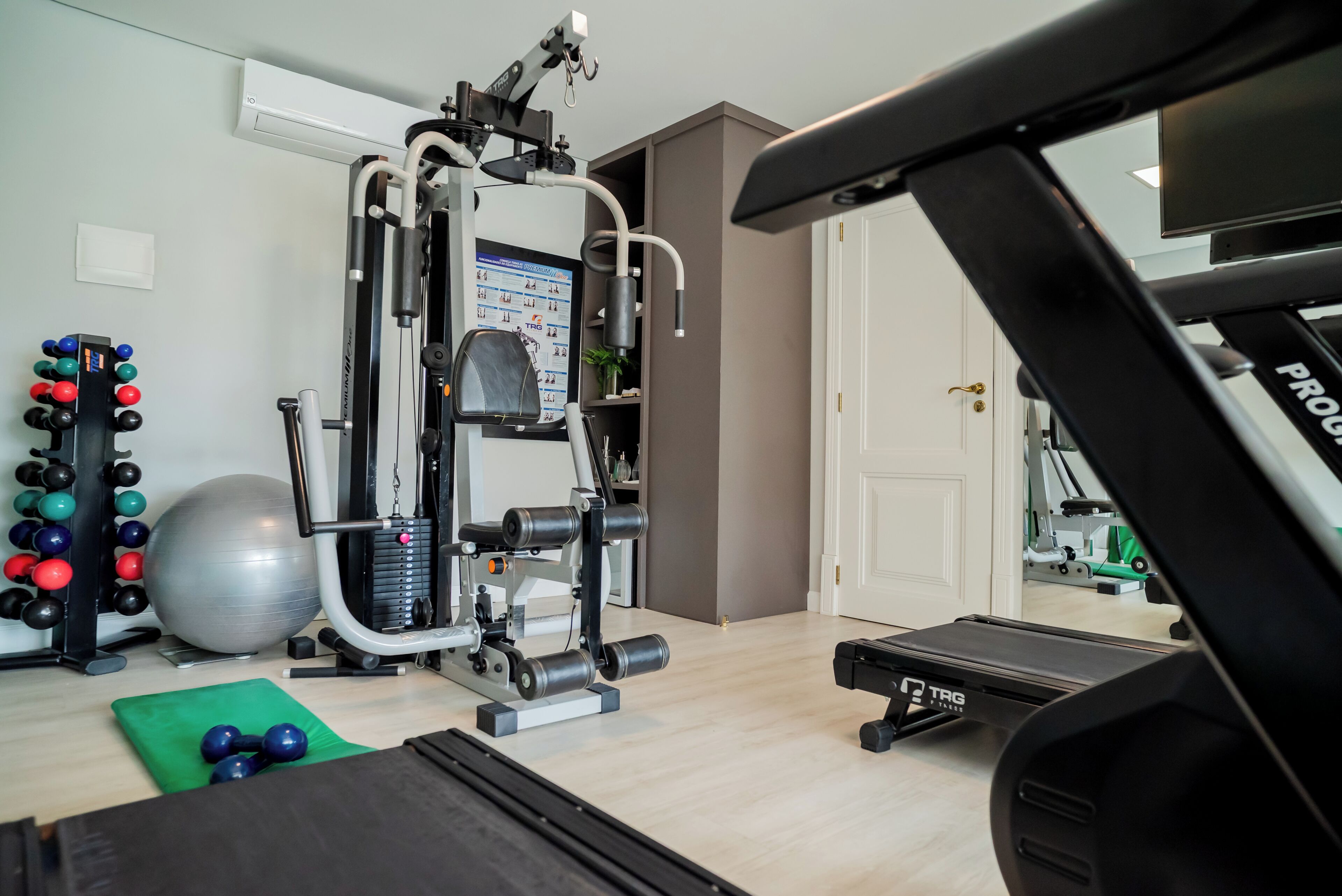 Un gimnasio en casa con equipo de ejercicio, una cinta de correr y un espejo que refleja la habitación.