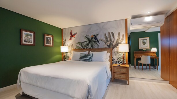 A hotel room with a large bed, a desk, a chair, and a wall with a mural. - Villa do Vale Boutique Hotel (Blumenau)
