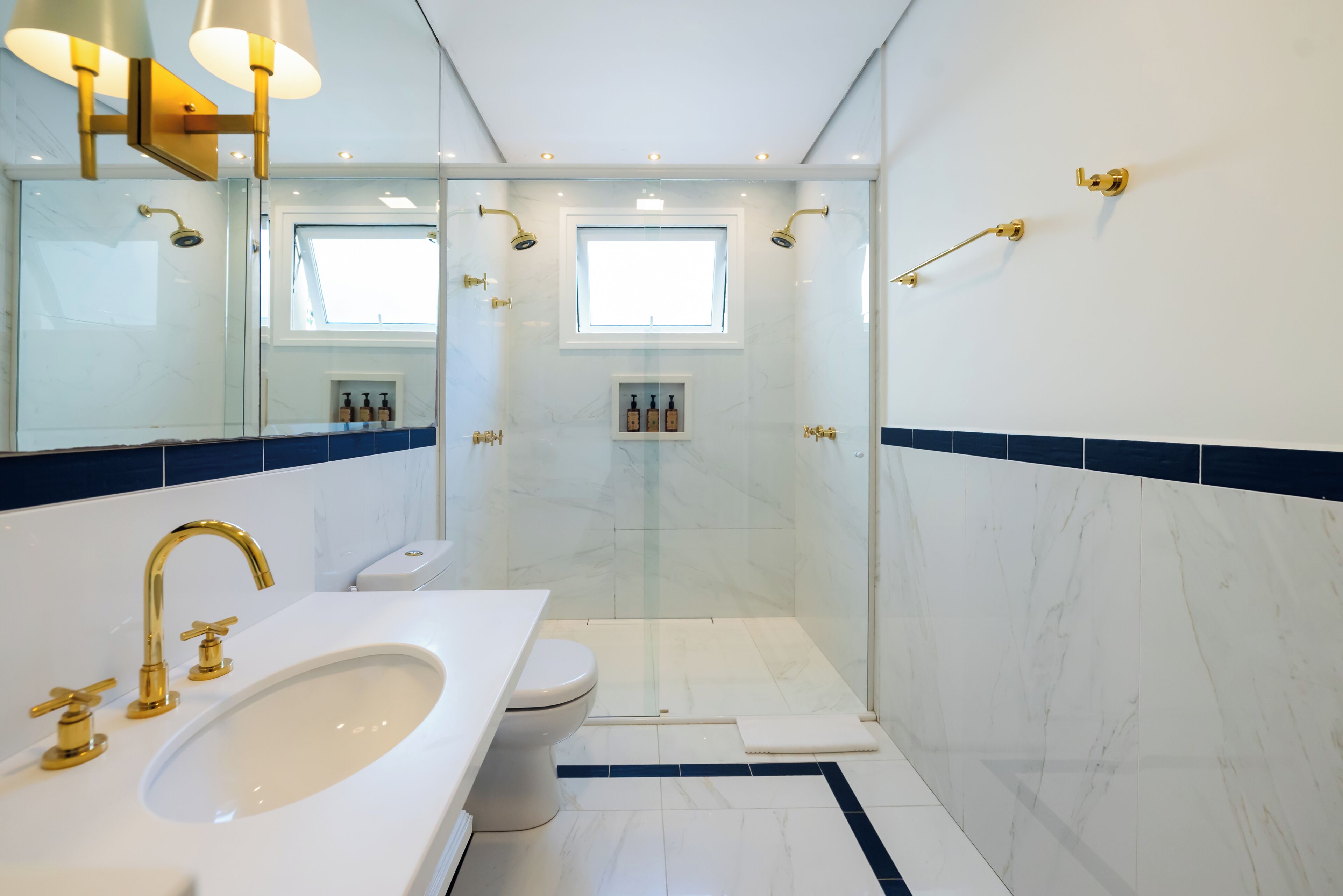A modern bathroom with a white sink, gold fixtures, a glass-enclosed shower, and a window.