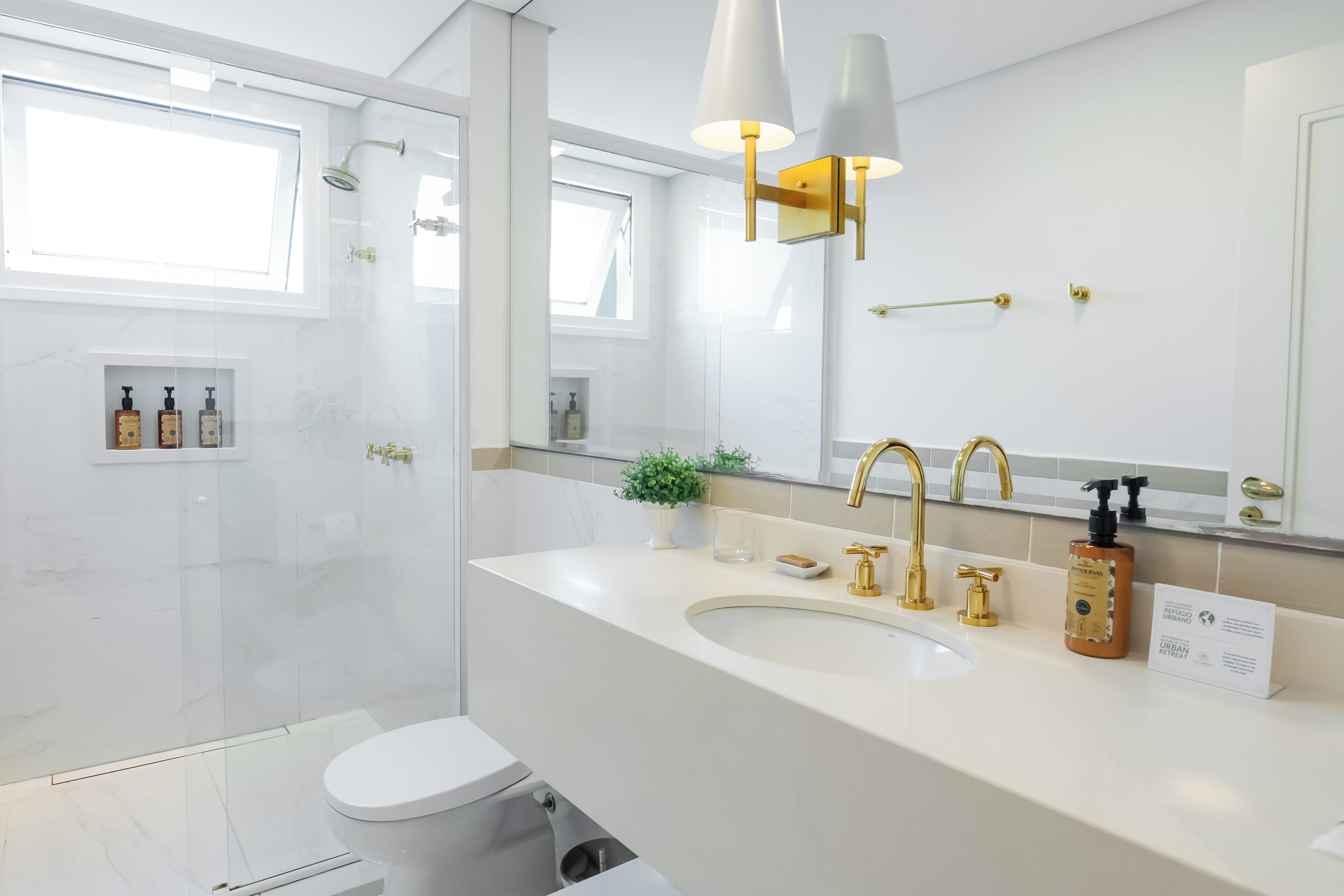 Un baño moderno con un espejo grande, un lavabo con detalles dorados y una cabina de ducha de vidrio.