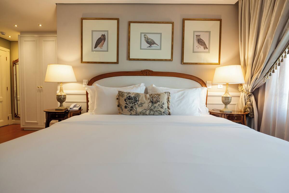 Una habitación de hotel con una cama grande, dos mesitas de noche con lámparas y tres obras de arte enmarcadas en la pared.
