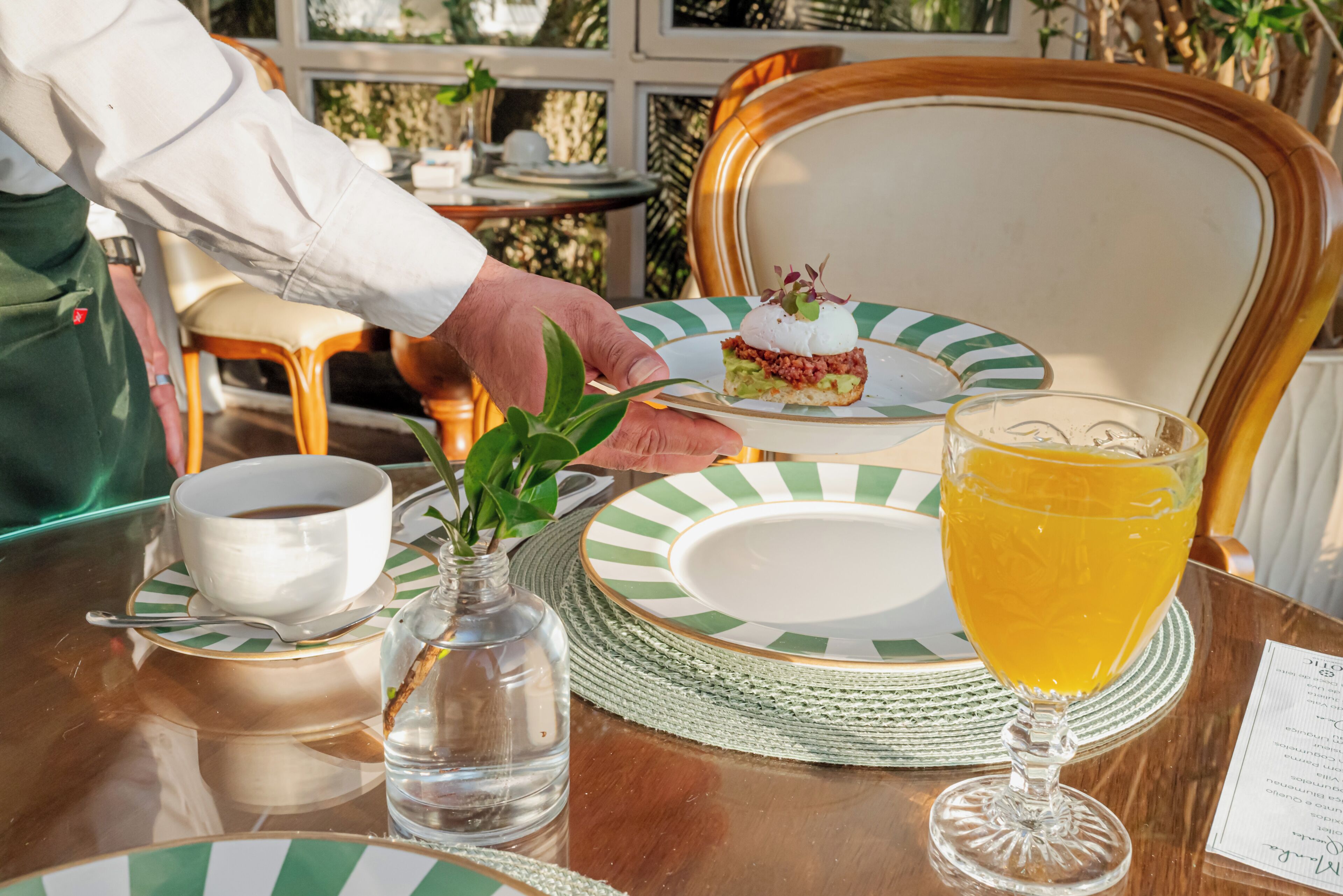 A table with a plate, a cup, a glass of juice, and a small vase with a plant.