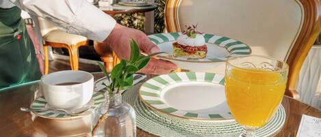 A table with a plate, a cup, a glass of juice, and a small vase with a plant.