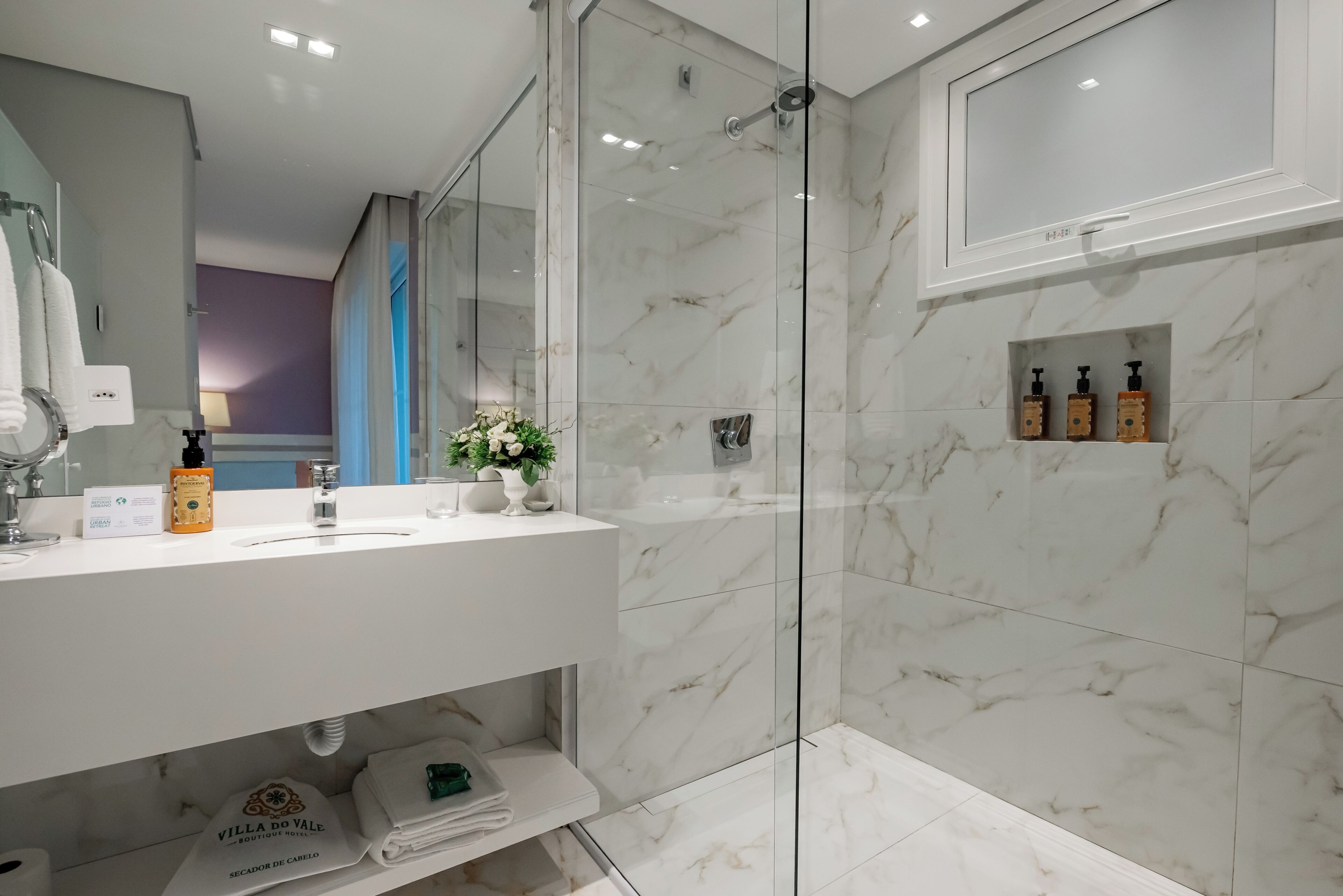 A modern bathroom with a glass-enclosed shower, a white vanity with toiletries, and a marble backsplash.