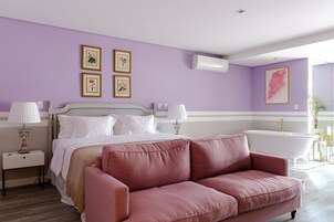 Un dormitorio con cama, un sofá rosa, una bañera blanca y aire acondicionado instalado en la pared.