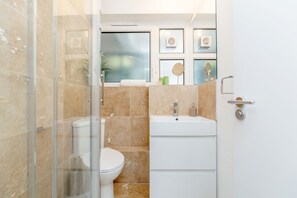 Un bany amb plat de dutxa de vidre, vàter i un lavabo amb mirall a la part superior.