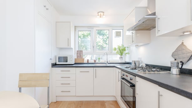 Une cuisine moderne avec des meubles blancs, un plan de travail noir, un four à micro-ondes, une cuisinière et une fenêtre donnant sur les arbres.