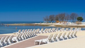 A beachside pool area with rows of white lounge chairs and a wooden pergola.