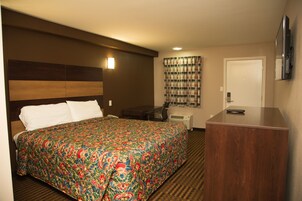 Habitación de hotel con una cama grande, un escritorio, una silla, un televisor y una puerta.