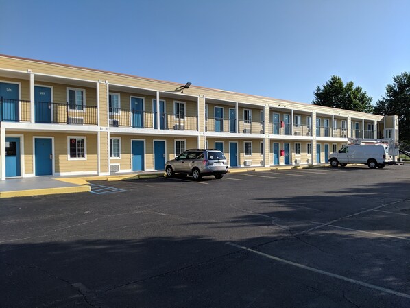 Un motel con varias habitaciones, un estacionamiento y un vehículo utilitario estacionado al frente.