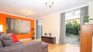 Ein Wohnzimmer mit grauem Sofa, einem großen Gemälde an der orangefarbenen Wand und einem Holzschrank.