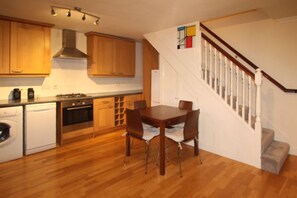 A kitchen with wooden cabinets, a stove, and a dining table with chairs. - Dunston (London)
