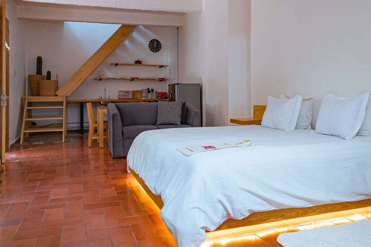 A bedroom with a bed, a desk, a chair, and a small kitchenette.