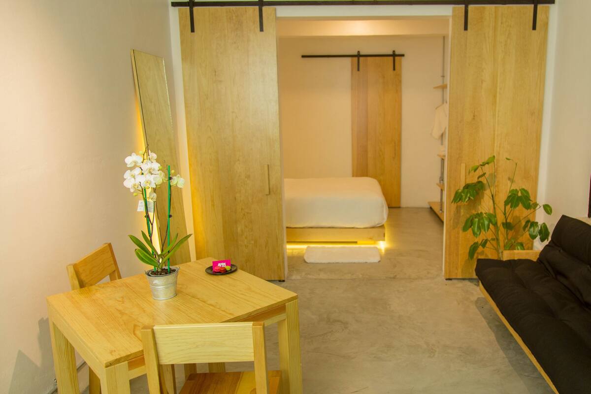 A compact room with a bed, a small table with a potted orchid, a black sofa, and a sliding door.