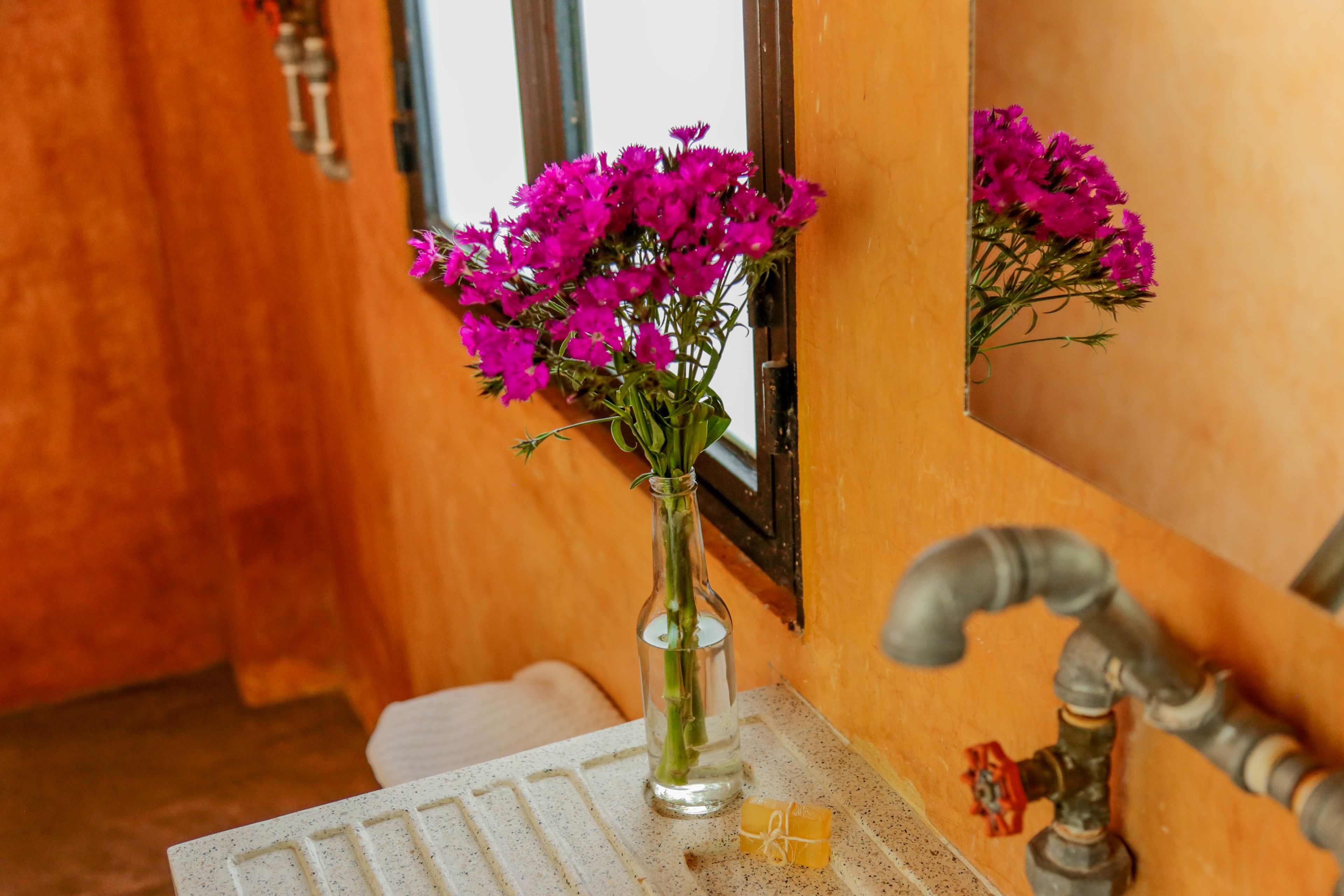 A bathroom with a wooden wall, a mirror, a sink, and a vase with purple flowers.